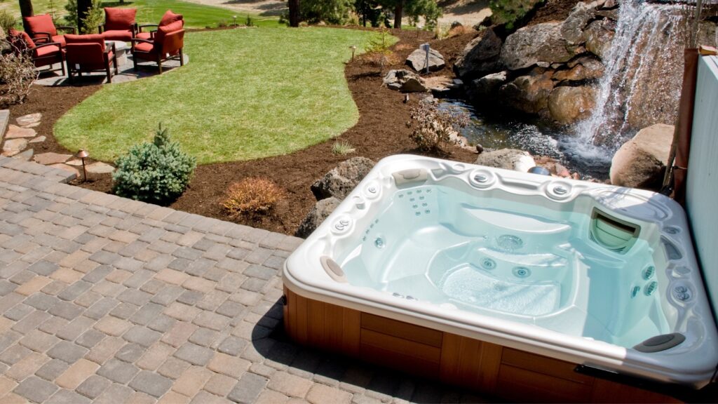 A hot tub on a pleasant patio overlooking a waterfall and beautifully landscaped garden.