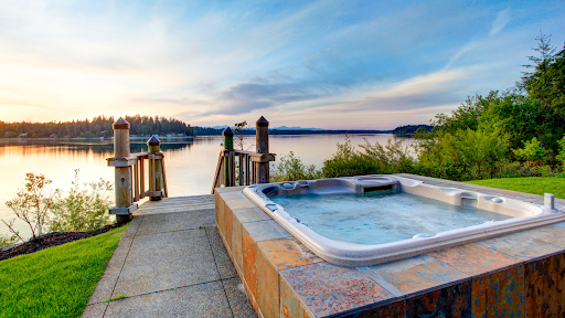 A hot tub sits on the edge of a large lake and a forest.