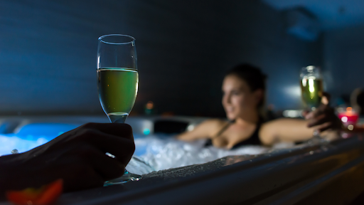 A couple drink champagne in a beautifully lit hot tub.